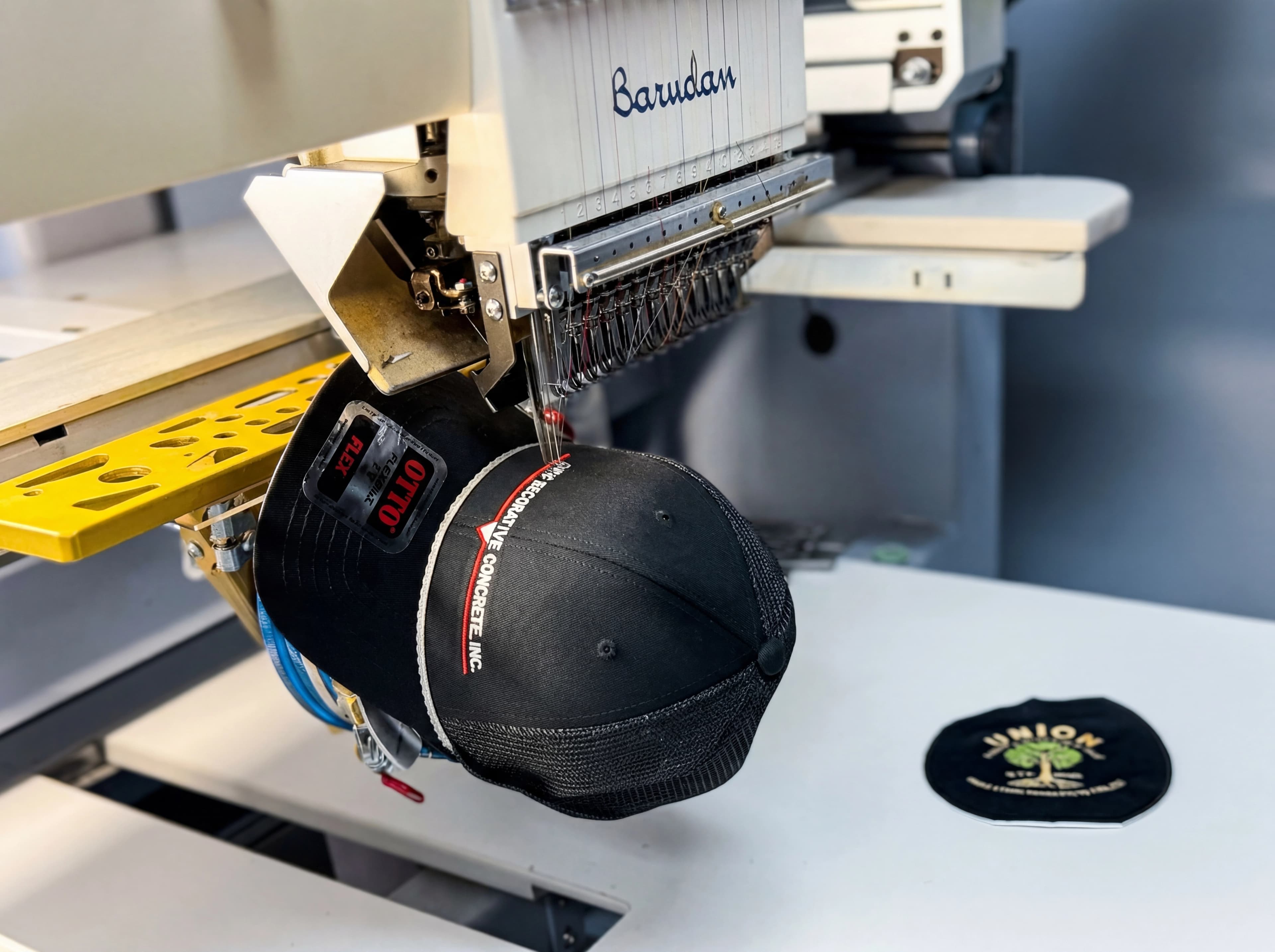Commercial embroidery machine stitching a custom black trucker hat